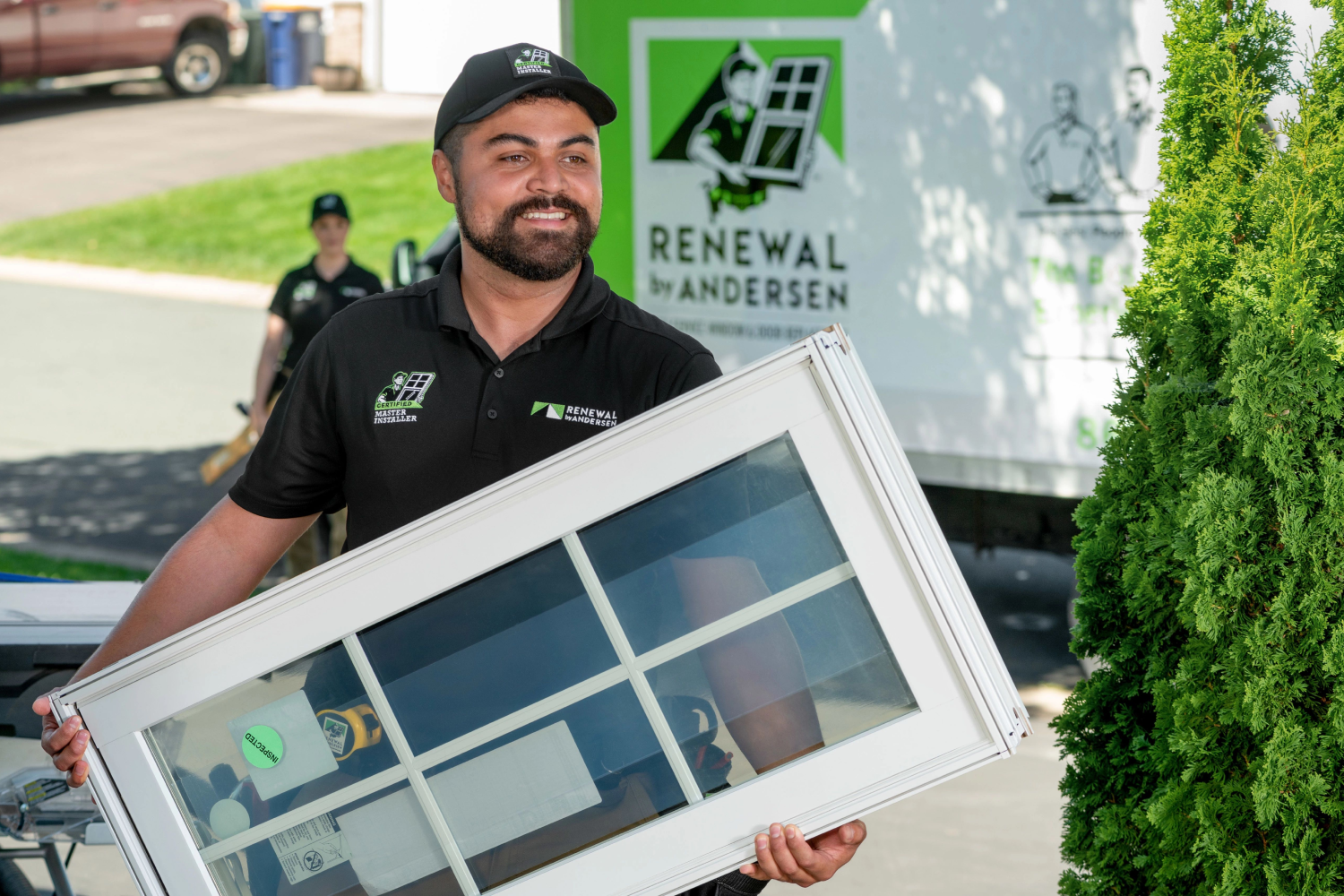 A Renewal by Andersen installer carrying a white window from a van into a homeowners house