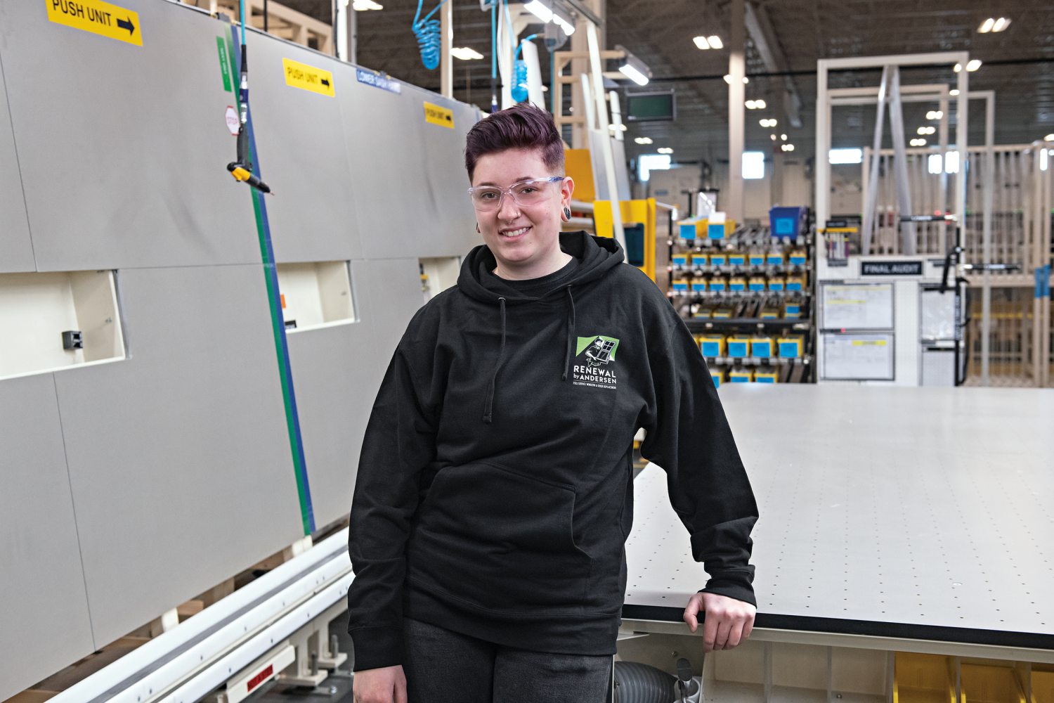 A Renewal by Andersen production associate standing in the middle of the factory next to a work station