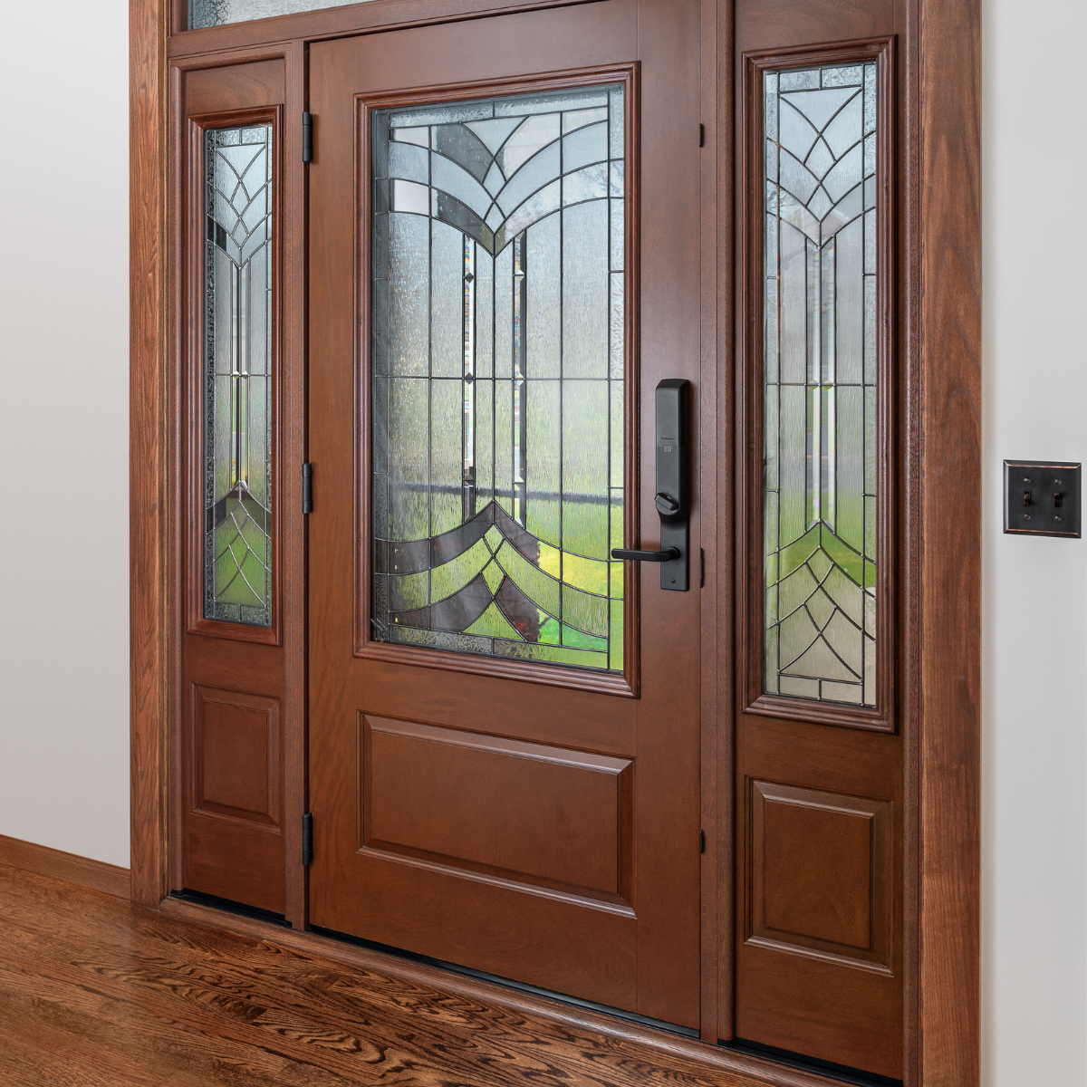 An Ensemble entry door with dual sidelights and artglass. The door and sidelight panel finish is a rich wood. There is black hardware.