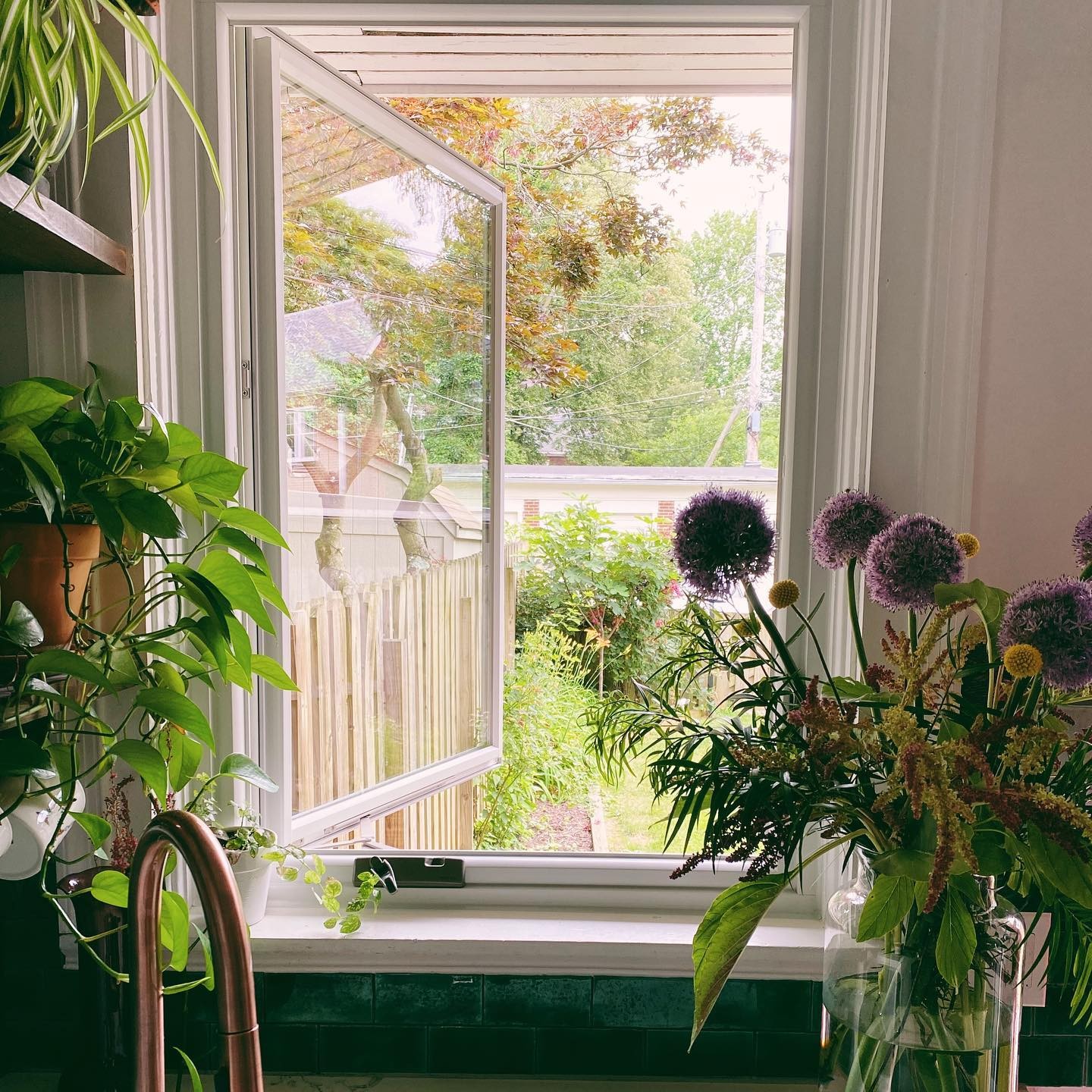 A casement window in a kitchen behind a sink. Flowers in front.