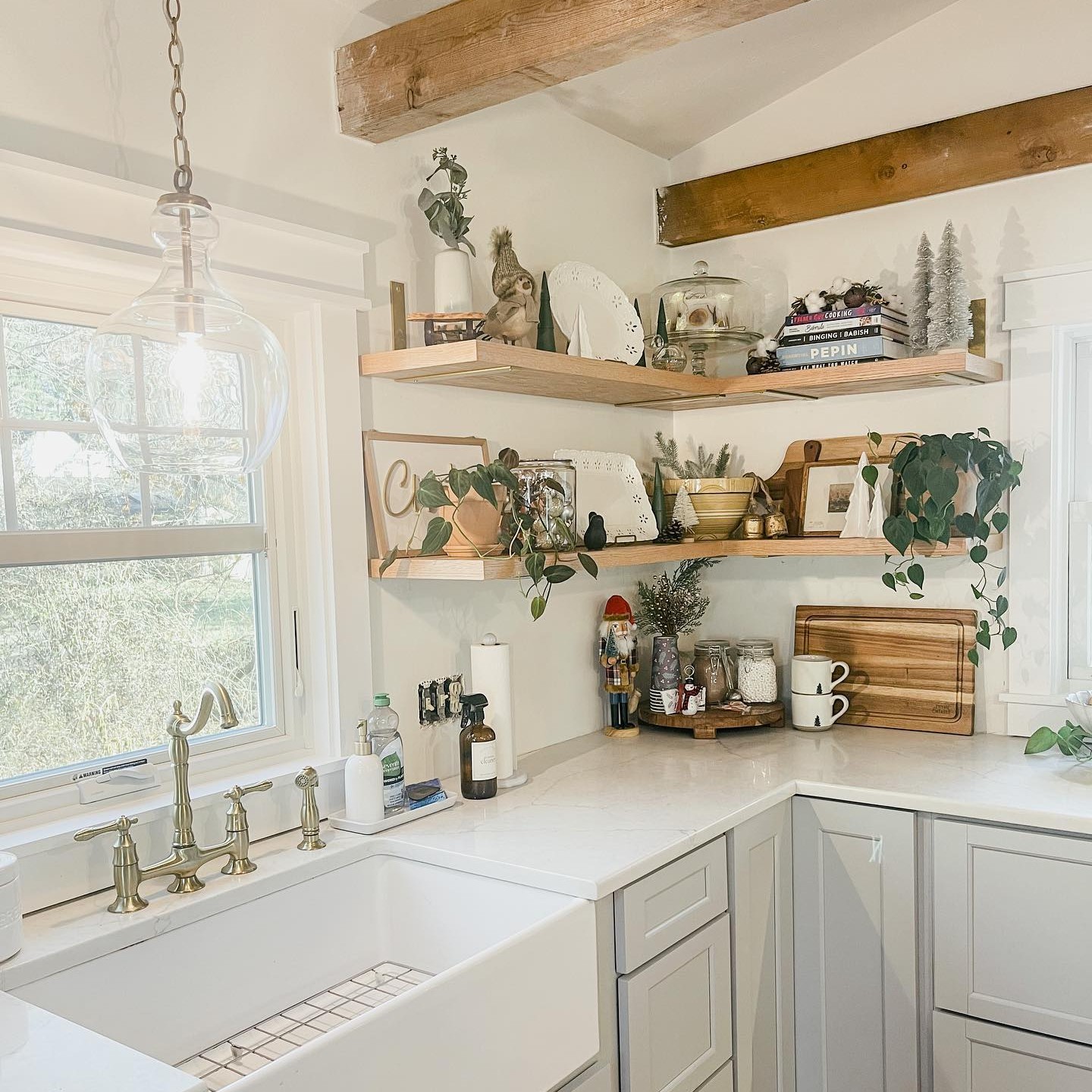 A white farmhouse style kitchen with rustic beams, a large sink, and a casement window behind the sink. The grilles are designed to make it look like a double hung window.