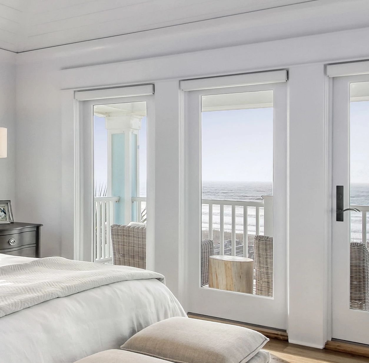 A bedroom with large picture windows looking outside to the beach.