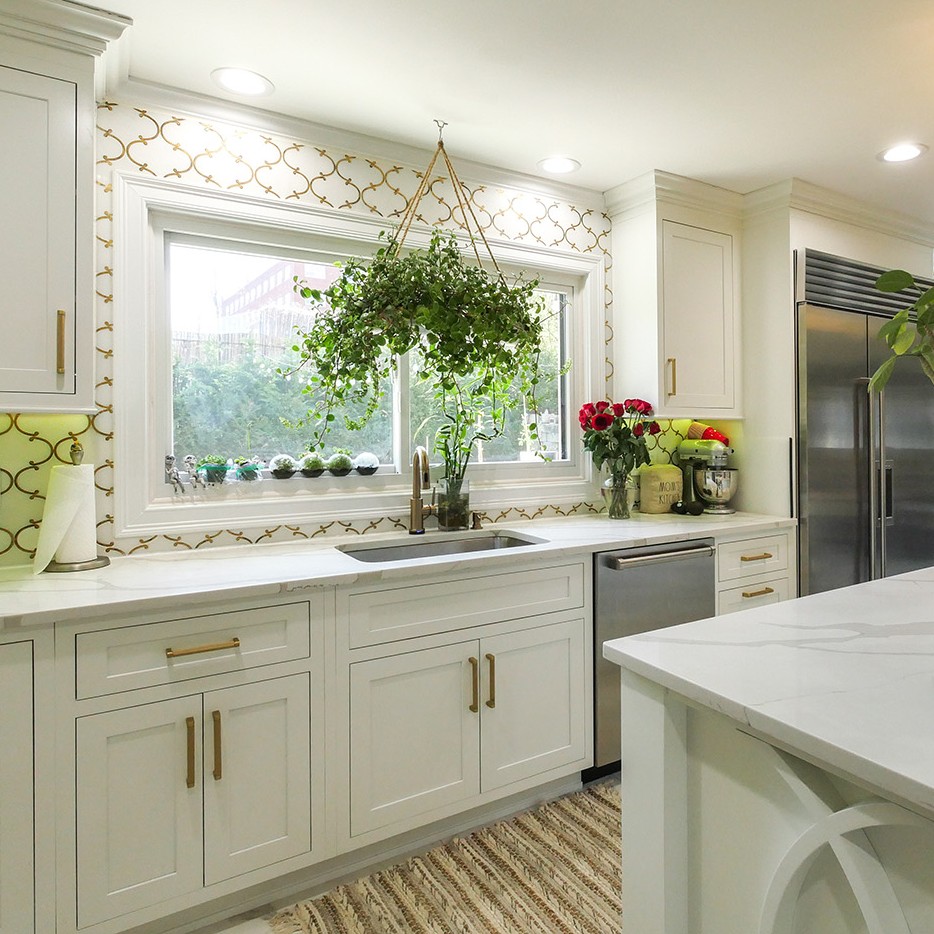 A bright kitchen with white cabinets. There are many plants in front of the gliding windows over the sink.